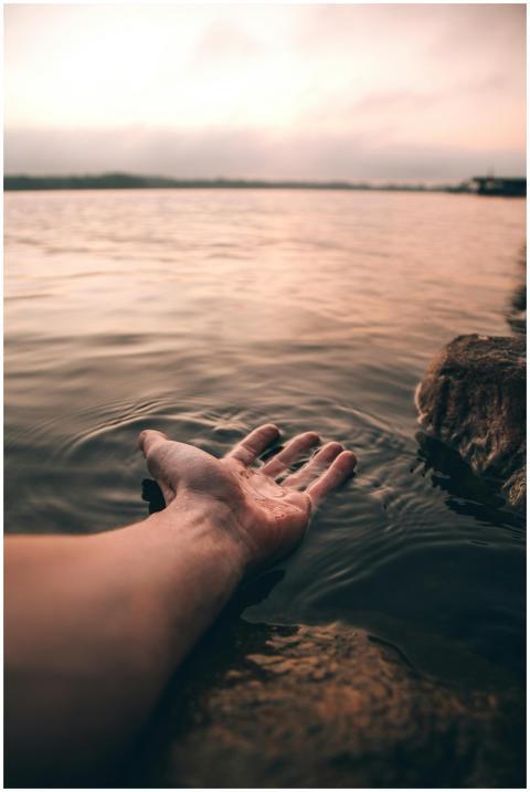 A serene image of a hand touching the water at twi