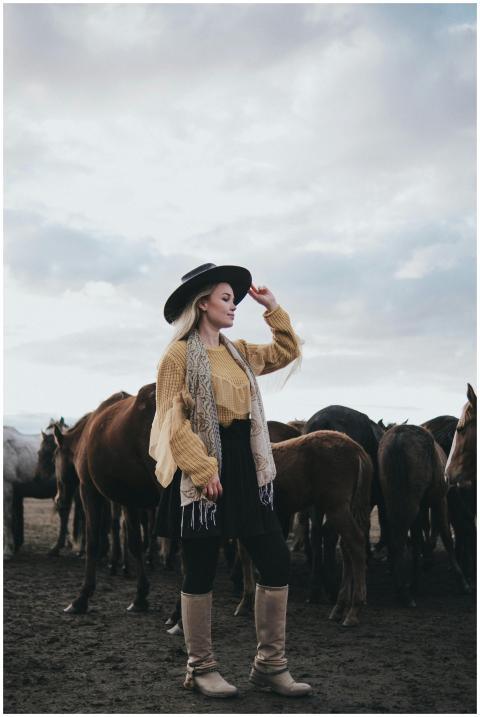 A stylish woman in a cowboy hat stands with a herd