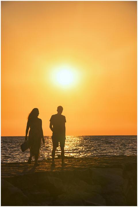 Silhouetted man and woman walking by the sea durin