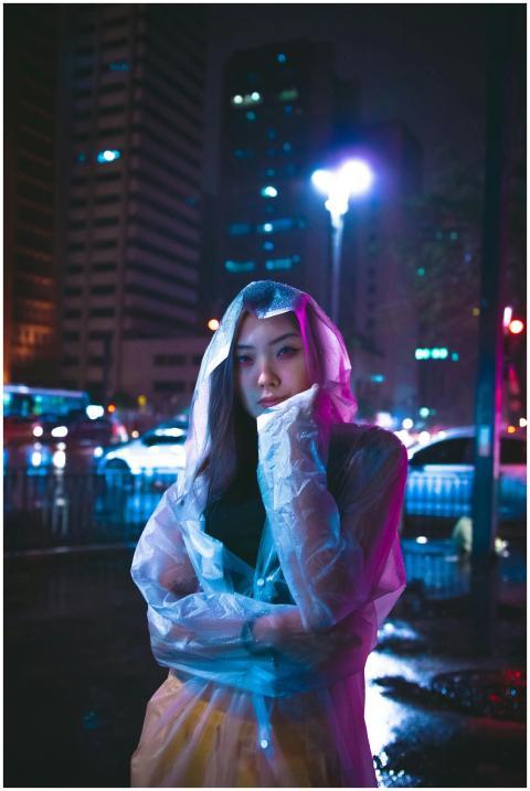 Woman in raincoat poses on city street at night wi