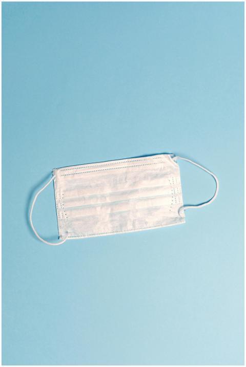 A disposable face mask on a light blue surface, sy