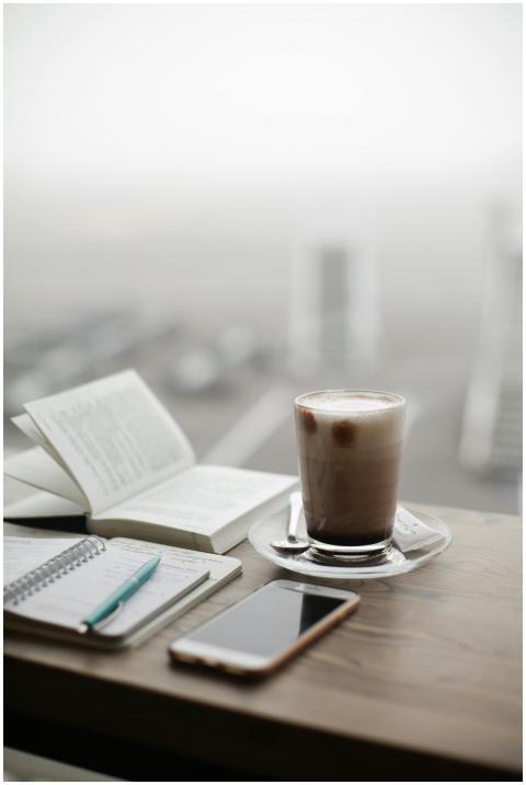 A warm coffee sits beside a notebook and smartphon