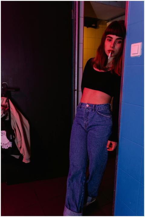 A young woman in casual attire leans in a doorway,