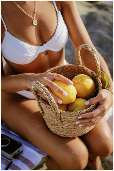 Woman in a white bikini holding lemons in a woven