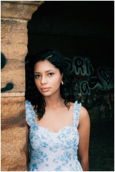 A young woman in a floral dress poses next to a gr