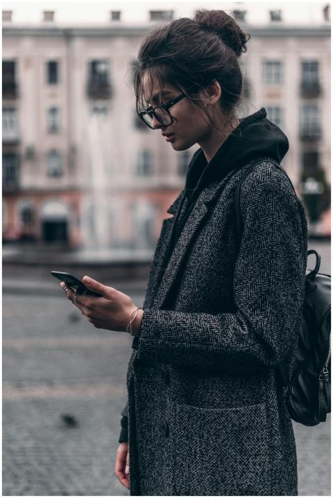 Fashionable young woman in coat using smartphone o