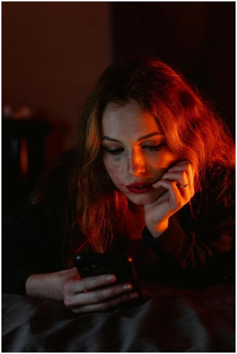 A woman with red hair lies indoors, expression tho