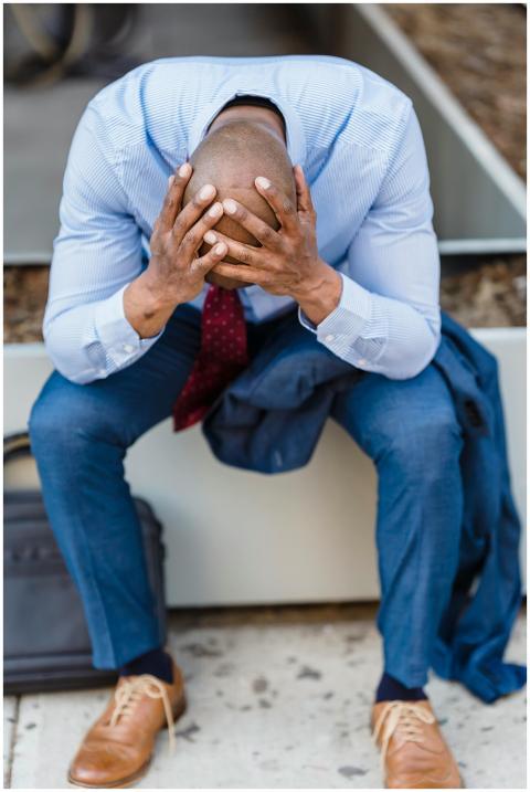 A businessman in a suit sits outdoors, head in han