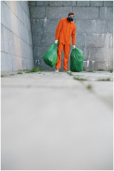 A waste collector in an orange suit holds green tr