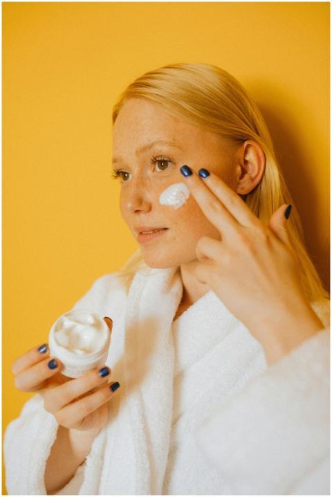 Woman in bathrobe applying skincare cream to face