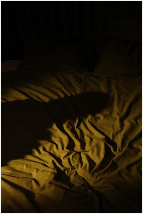 A dark bedroom with crumpled bedsheets and a myste