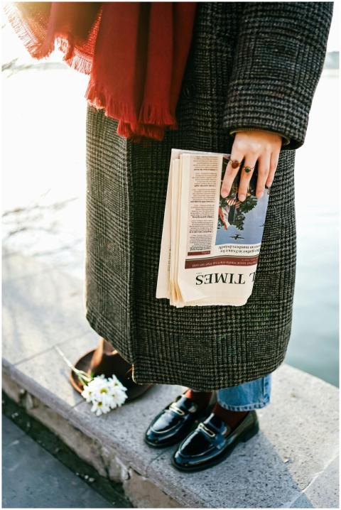 Fashionable woman in coat holding a newspaper near