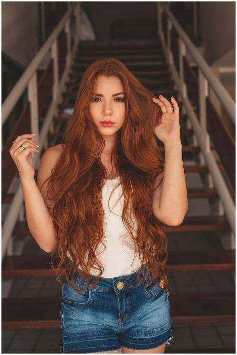 A stylish woman with long red hair poses on stairs