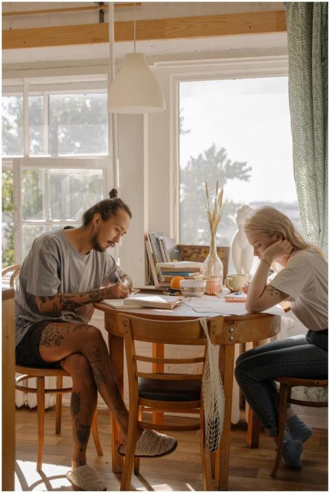 Two young adults engage in study at a sunlit table
