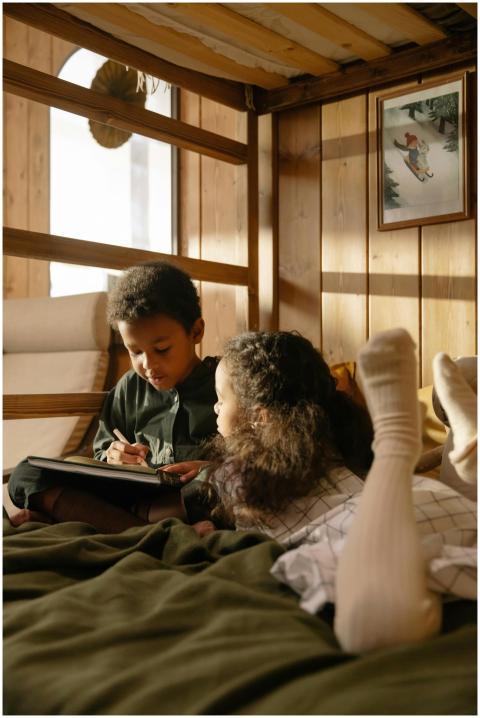 Two children drawing together on a bed in a warm,