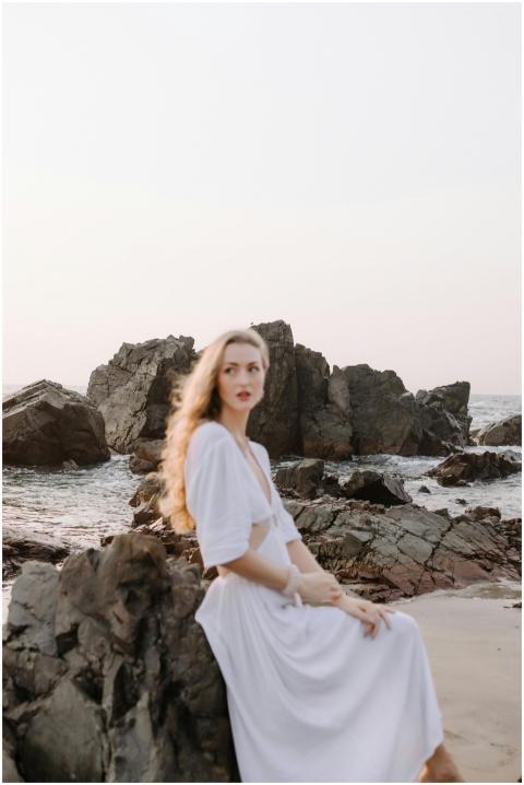 Elegant woman in a white dress sits by rocks at a