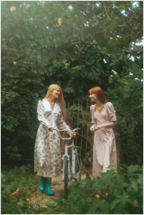 Two women in long floral dresses share a light mom