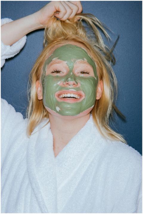 Woman in a bathrobe smiling while applying a green