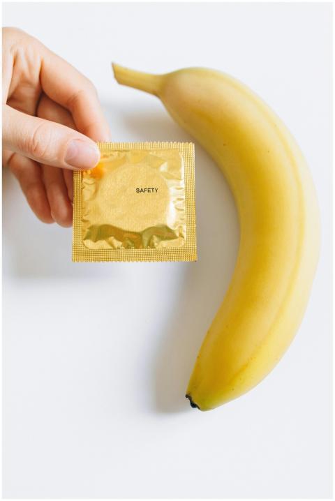 Close-up of a hand holding a condom package beside
