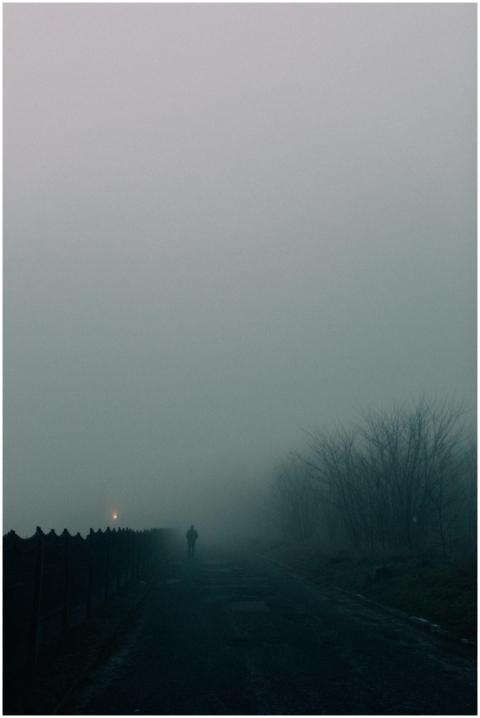 A solitary figure walks down a fog-covered road, c