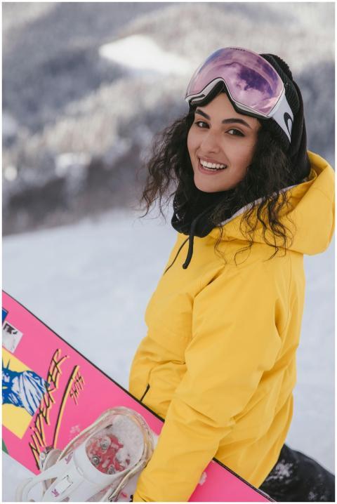 Smiling woman in yellow jacket with pink snowboard