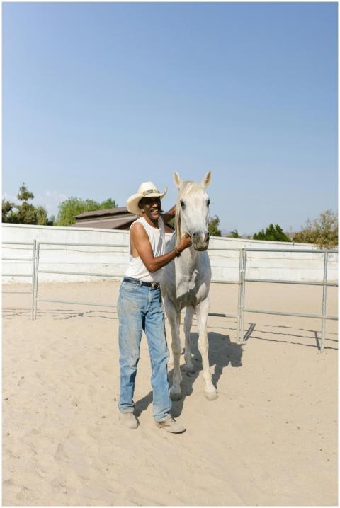 Man in cowboy attire with a horse at a sandy ranch