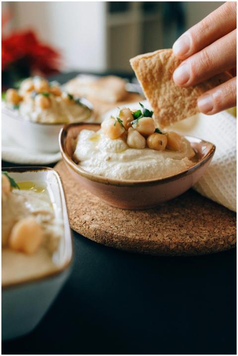 Close-up of a hand dipping pita bread into creamy