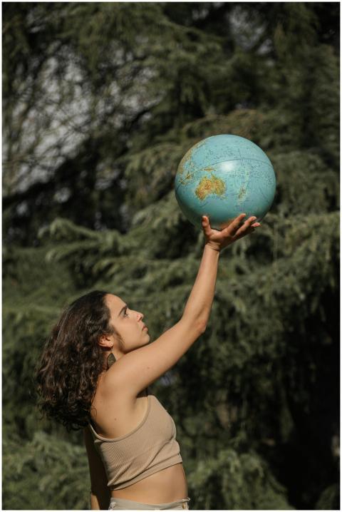 A woman holds a globe high outdoors, symbolizing g