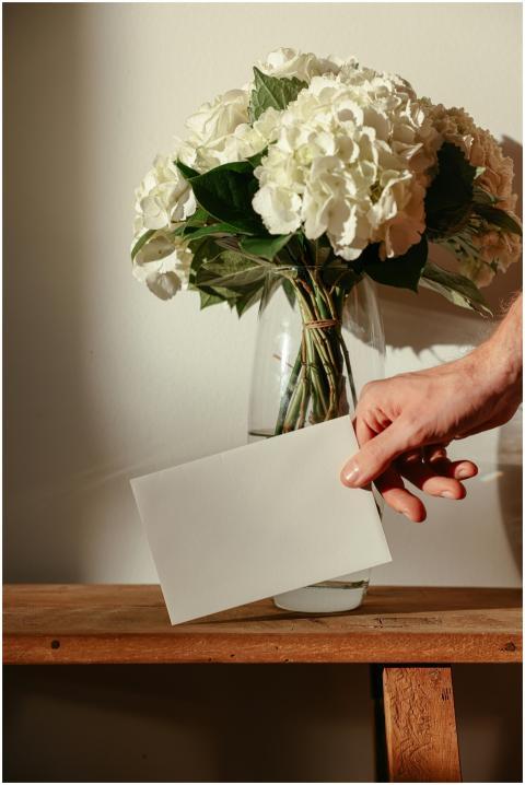 A hand holding a card next to a vase of white flow