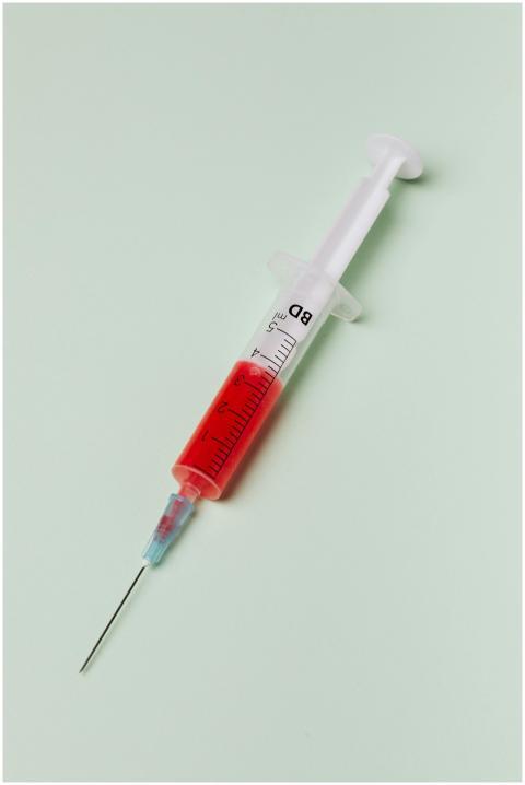 Close-up of a syringe with red liquid on a light g