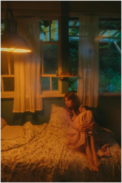 Woman in a tranquil bedroom, wrapped in warm light