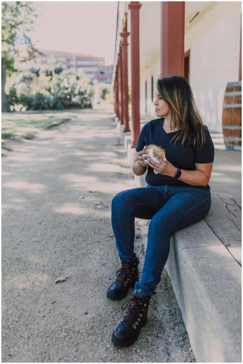 A woman sits outdoors enjoying a sandwich in a pea