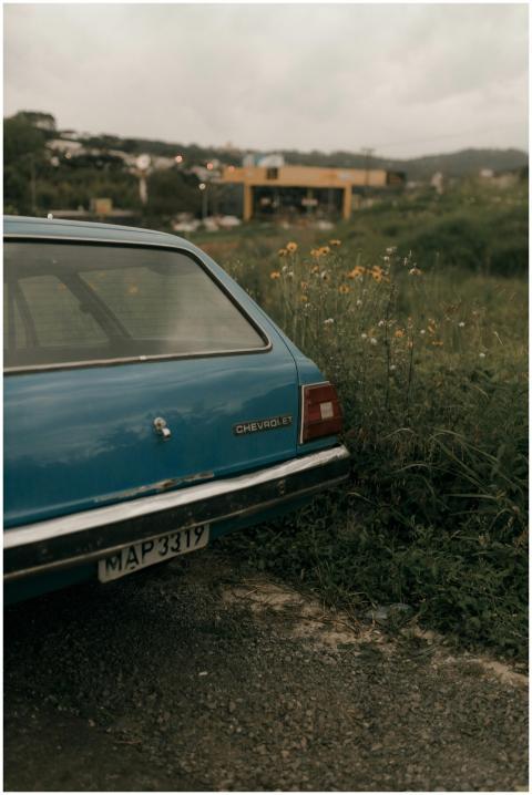A classic blue car parked in a grassy, rural area