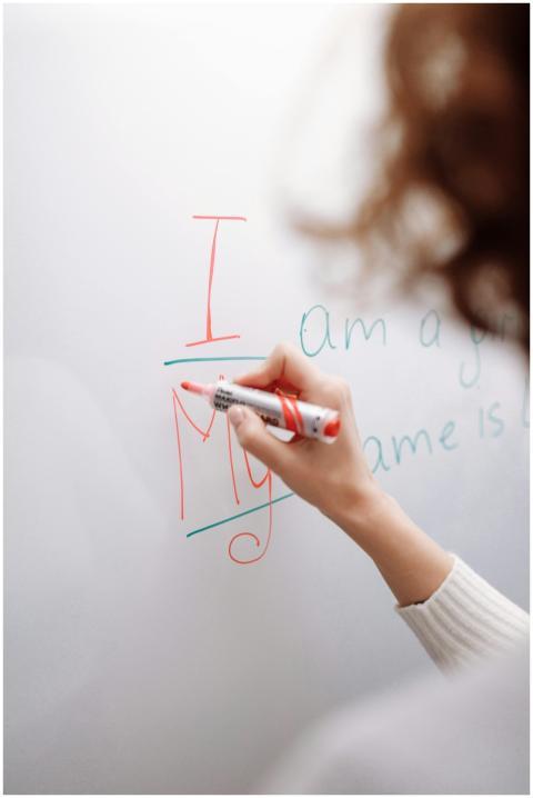 A hand with a marker writing on a whiteboard indoo