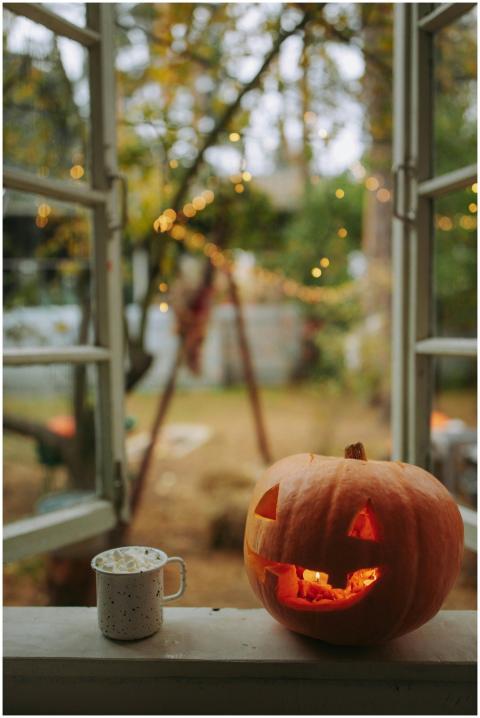Halloween pumpkin and cozy mug on a window sill wi