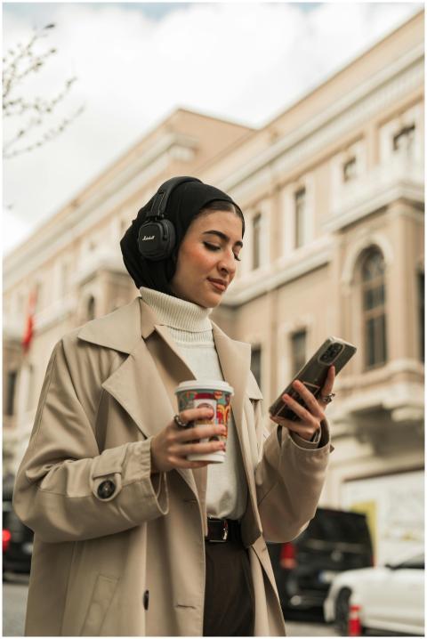 Stylish woman in beige coat enjoys coffee and musi