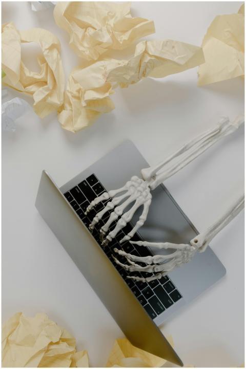 Skeleton hands on a laptop surrounded by crumpled