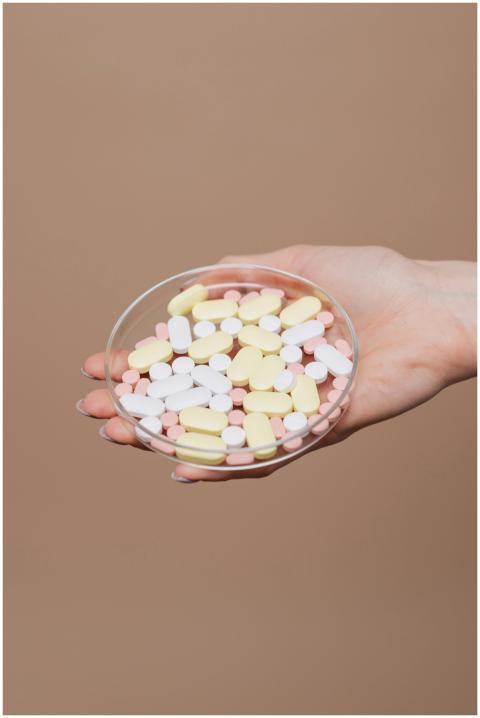 A hand holding assorted pills in a petri dish, sym