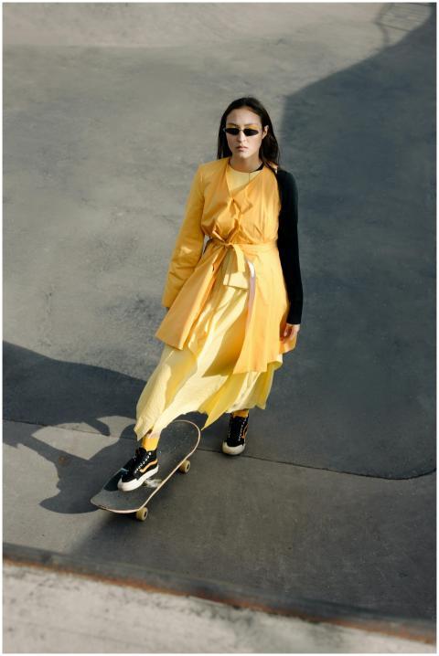 Fashionable woman in yellow dress skateboarding at