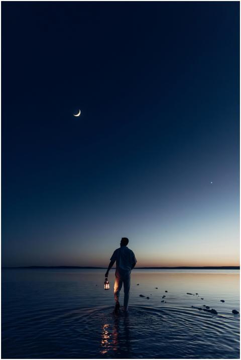 Silhouette of a man holding a lantern walking on w