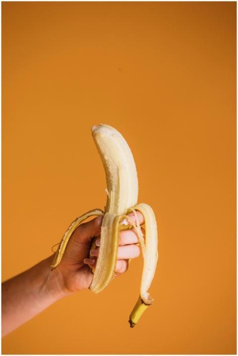 A peeled banana held in hand against a vibrant ora