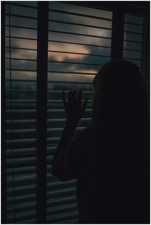 Moody silhouette of person peering through blinds
