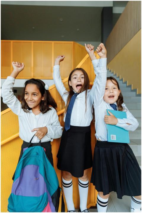 Three cheerful schoolgirls in uniforms celebrating