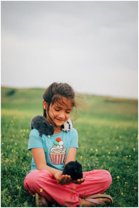Cheerful child sitting outdoors with rabbits, enjo