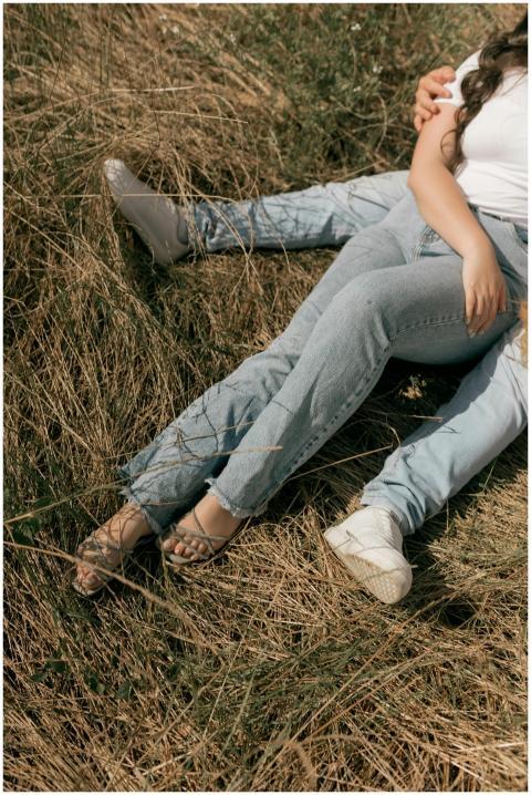 Couple in jeans lying on dry grass outdoors, showi
