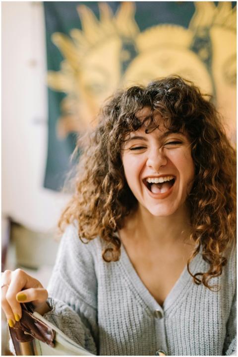 Happy woman with curly hair laughing indoors, expr