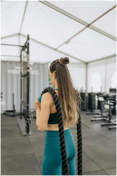 Fit woman in activewear using battle ropes indoors