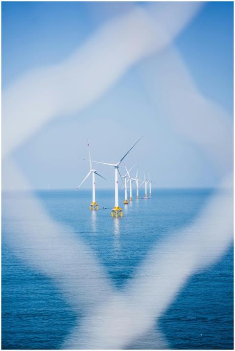 A row of offshore wind turbines standing in calm b