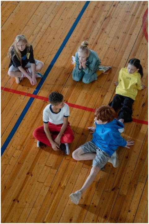 Group of diverse children sitting on gym floor, en