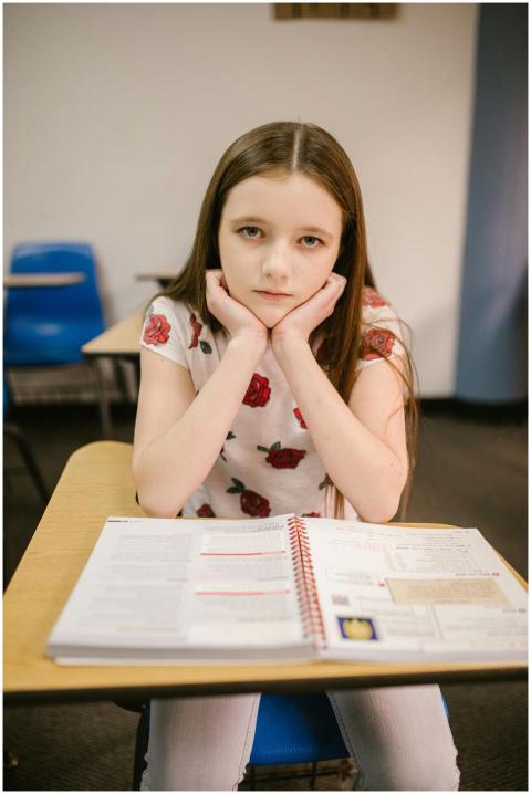 Pensive young girl sitting alone with textbook in
